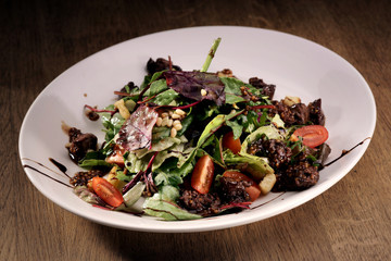 Fresh green salad with cherry tomatoes and beef served on a white plate on wooden rustic counter
