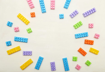 Frame of toy colored plastick bricks on light wooden background