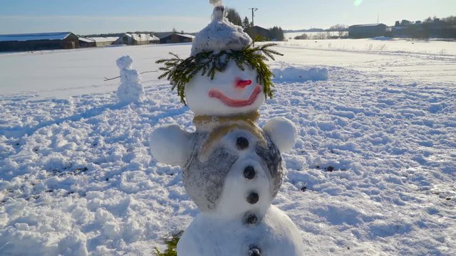 The small snowman with grasses on the head scarf on the neck and black buttons on the middle body