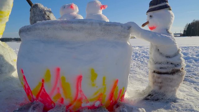 A snow sculpture of the big pot with fire with a snowman holding the pot