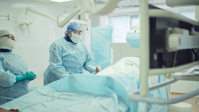 Female surgeon looking at monitors while performing coronary artery bypass graft assisted by nurse in modern operating room, shot on Sony NEX 700 + Odyssey 7Q