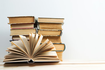 Open book, stack of hardback books on wooden table. Back to school. Copy space