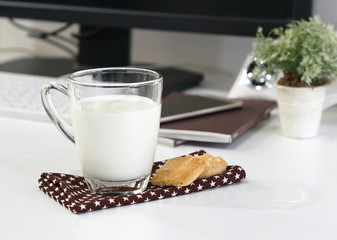 Glass of milk with cookies on cloth and white table in office room