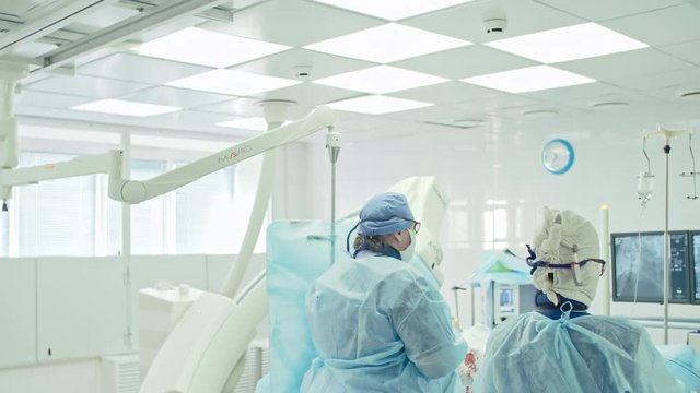 Tracking shot of surgeon and nurse looking at monitors during coronary artery bypass surgery in modern operating room, shot on Sony NEX 700 + Odyssey 7Q