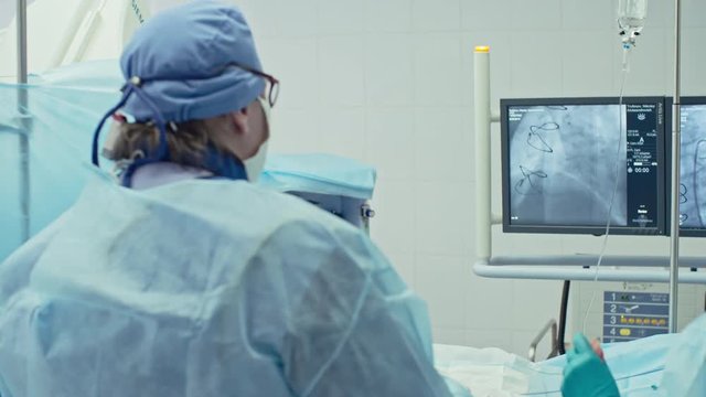 Rear view of female surgeon looking at monitors while performing coronary artery bypass graft in modern operating room, shot on Sony NEX 700 + Odyssey 7Q