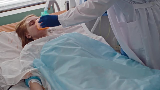 Doctor adjusting oxygen mask on face of female patient lying in bed in intensive care room, shot on Sony NEX 700 + Odyssey 7Q