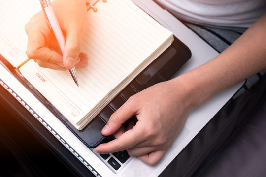 female hands with pen writing on notebook with laptop.