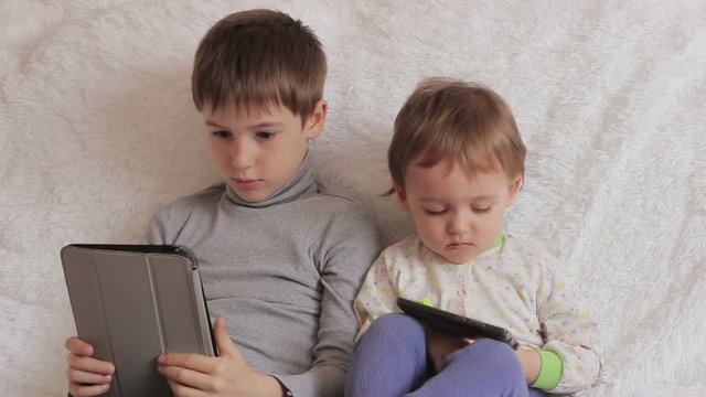 Children sitting on the couch playing on your tablet and phone to computer games