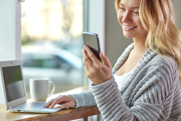 Beautiful young woman working on laptop and holding a phone at the cafe