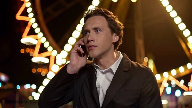 Handsome businessman talking on his smartphone angry with amusement park on a background. Slow motion