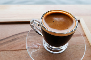 Hot espresso in clear glass cup and saucer on wooden tray, outdoor scene