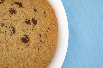 Top close view of a gluten-free chocolate chip cookie on a white plate atop a blue tablecloth