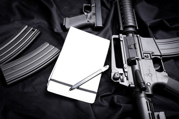 Rifle, gun, knife with sheath, compass and notebook with pen on on black cloth