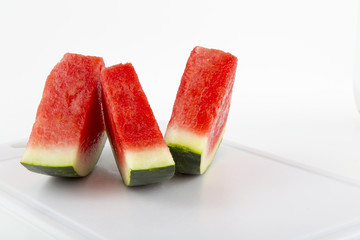 Three slices of watermelon setting vertical on a white cutting board and white background