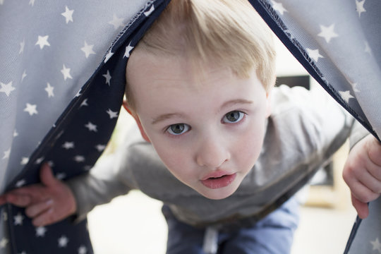 Portrait of boy peeping into a tent at home