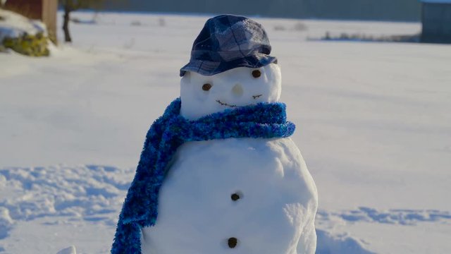 The cute smiling snowman on his blue cap and his blue scarf on his neck
