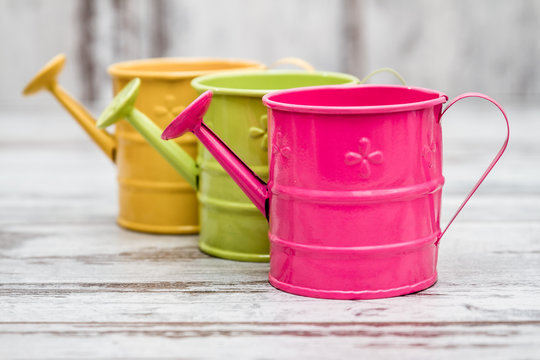 Simple Colorful Metallic Watering Cans on White Woodeen Background