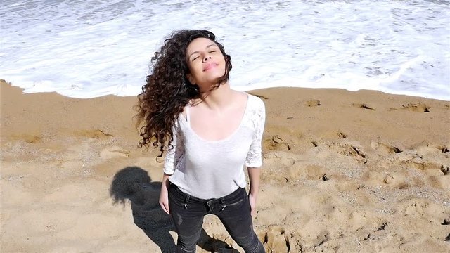 Slow motion of happy young woman with beautiful curly hair enjoying the summer sun on the sea shore, low angle shot