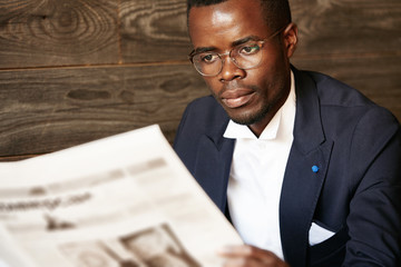 Close up portrait of serious black corporate worker in formal two-piece suit and spectacles holding...