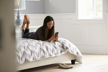 Obraz premium Woman Relaxing On Bed Checking Mobile Phone