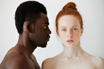 Coffee and milk. Portrait of young mixed race couple posing naked against white studio wall. Profile of African man looking at his Caucasian girlfriend with love and affection. Interracial relations
