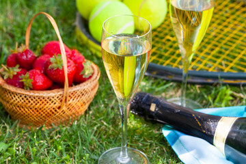  Strawberries, champagne and tennis balls on racket in the grass