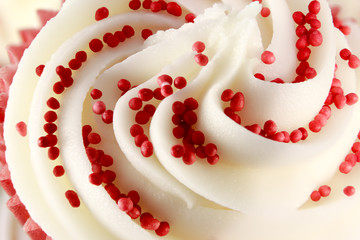 Closeup of red velvet cupcake decorated with swirled icing and sugar beads