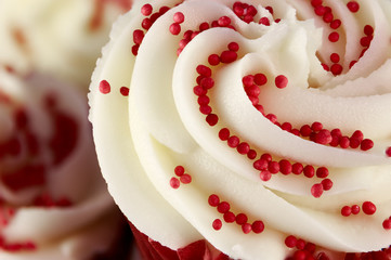 Closeup of red velvet cupcake decorated with swirled icing and sugar beads