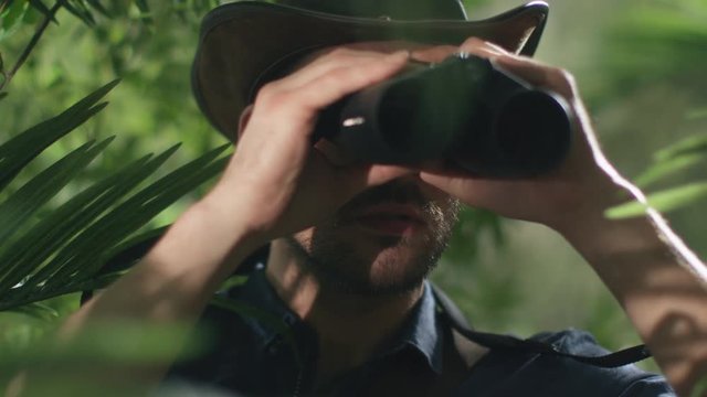 Adventurer in Hat Walking through Jungle Forest And Looking through Binoculars. Shot on RED Cinema Camera.