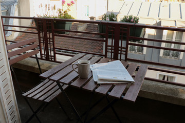 Meeting morning on the balcony with coffee and newspaper, view on roofs, potted flowers.