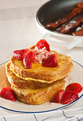 French toast with fresh strawberries and grilled bacon in background