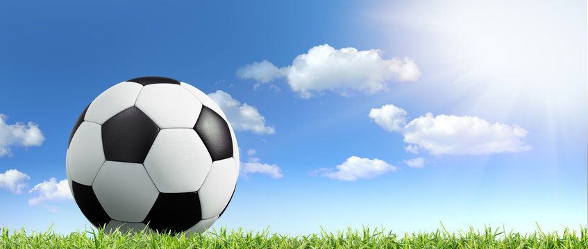Fußball im Gras vor blauem Himmel mit Sonne und Wolken