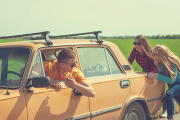 Young hipster friends on road trip on a summers day. Engine break down.Two girls pushing a vintage...