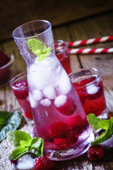 Raspberry drink with berries and ice in a glass pitcher on a dar
