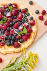 Fresh berries on the tart cake from above. Delicious homemade pie with organic raspberries and blueberries and summer flowers on wooden board. Summer dessert and snack.
