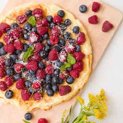 Fresh berries on the tart cake from above. Delicious homemade pie with organic raspberries and blueberries and summer flowers on wooden board. Summer dessert and snack.