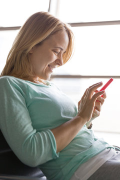 Close up photo of beautiful young woman sitting cozy at the airport and waiting for her glight. Girl using  touch screen smartphone. Typing on the telephone. Ready for vacations.