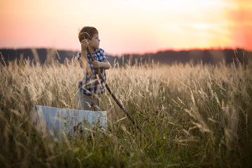 Boy seaman floats on a sailing boat in the field at sunset on a warm evening summer. Dreams of travel! Child floats on a handmade boat against the backdrop of a sunset.