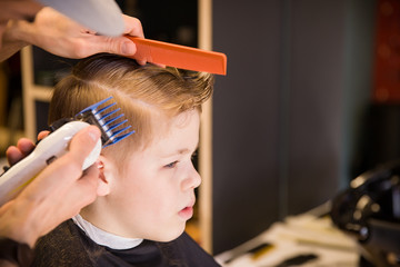 Close-up of man hands grooming kid boy hair in barber shop. Boy cut with hairdresser's machine....
