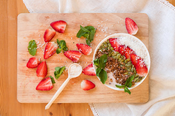 Breakfast berry smoothie bowl topped with strawberry, pumpkin seeds, coconut, muesli and fresh mint. Strawberry banana smoothie bowl. healthy breakfast or snack, wooden tableware.