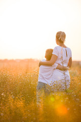 Beautiful young woman with her son on the daisy meadow on a sunny day. Happy family on summer...