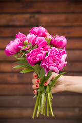 Beautiful bouquet of dark pink peonies in woman hands on a wooden background. Bunch of flowers in hands. Stripes. Summer time.