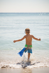 Happy boy in flippers running into ocean on a sunny day. Child going to swim in the sea. Vacations. Activities for child on the beach. Joy and happiness. © goodmoments