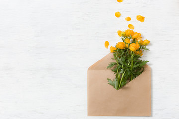 Top view on beautiful yellow garden flowers in the craft envelope on the white wooden background. Bouquet of flowers. Card. Greetings. Holidays and spring concept