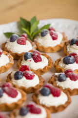 Closeup of delicious homemade cupcakes with vanilla cheese cream and organic blueberries and raspberries on the top served with fresh mint. Healthy dessert for celebration or party.