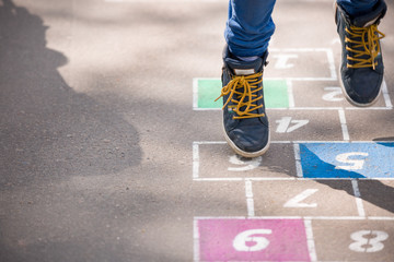 Closeup of boy's legs and hopscotch drawn on asphalt. Child playing hopscotch on playground...