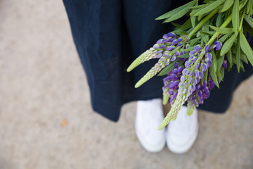 Closeup of woman's hands holding blue flowers lupine outdoors. Woman with wild flowers bouquet walking in the park.