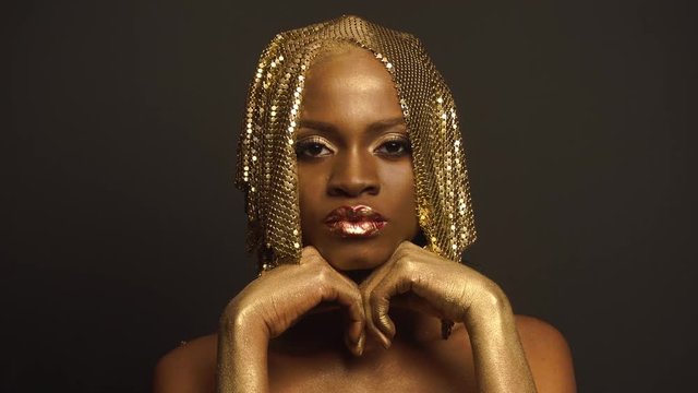 Big close-up portrait of surreal mysterious black african american female model with golden faceart and big glossy lips. Creative surreal concept