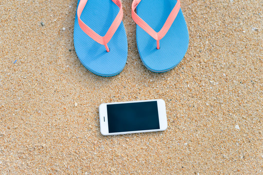 Top view close up on mobile phone flip flops on summer beach background. Happy joyful vacation