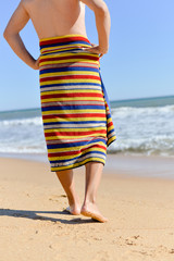 Person wearing towel walking along sand beach, closeup ol legs. sunny background outdoors